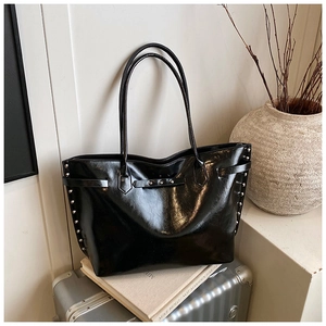 Close-up of black glossy tote bag with silver studs and belt buckle details on books