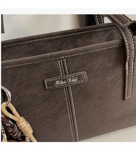 Detail of dark brown faux suede tote with contrast white stitching and woven pendant
