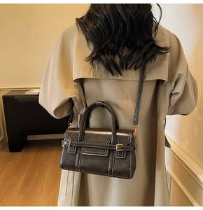 Dettaglio borsa vintage in pelle con cuciture bianche e fibbia dorata su un trench coat