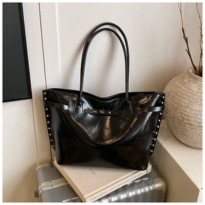 Detail of silver rivets on black glossy leather tote bag against minimalist background