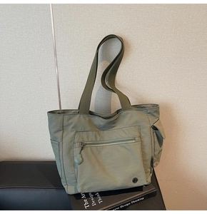 Detail view of large grey-green nylon tote bag with front zipper pocket and side slots