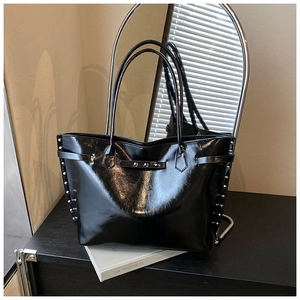 Detail of glossy black tote bag featuring silver rivet studs and dual shoulder straps