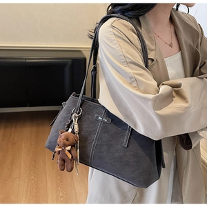Close-up of charcoal gray suede tote bag featuring contrast stitching and bear keychain