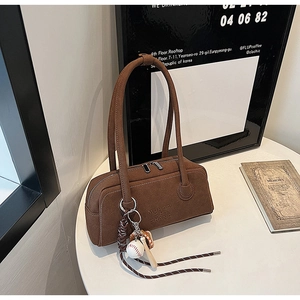 Detail of a brown suede shoulder bag with dual zippers and a baseball charm accessory