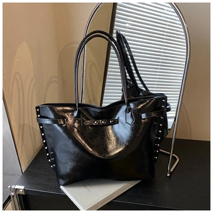 Close-up of black glossy patent leather tote bag with silver rivet details and slim handle