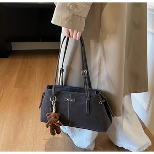 Detail of dark brown tote bag featuring white contrast stitching and a plush bear charm