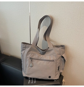 Detail of grey nylon tote bag with multiple pockets and metal logo on leather sofa