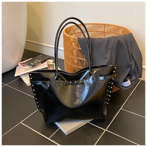 Detail shot of black patent leather tote bag featuring silver studs and buckle strap