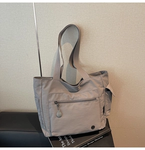 Detail view of grey nylon tote bag showing front zipper pocket and wide woven strap