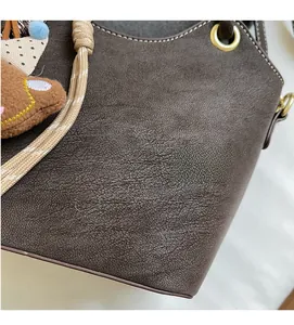 Close-up of brown textured leather bucket bag with woven handle and cute bear charm