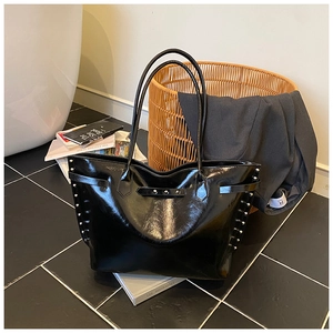 Detail showing silver rivets on a glossy black leather tote bag in a lifestyle setting