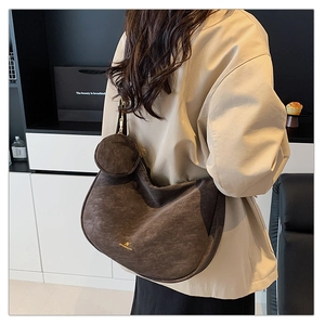 Detail of dark brown matte suede shoulder bag featuring a crescent silhouette and brand logo