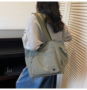 Detailed view of olive green nylon tote bag featuring front zip and flap pockets