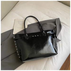 Detail shot of black patent leather tote bag with silver rivets and glossy finish