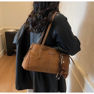 Close-up of brown faux leather tote bag with white stitching and plush bear charm
