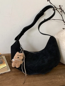 Vintage black suede hobo bag with a plush bear charm on a wooden table setup