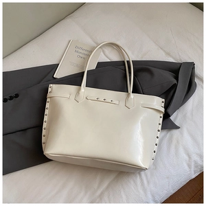 Detail view of cream tote bag with silver metal studs and glossy faux leather texture
