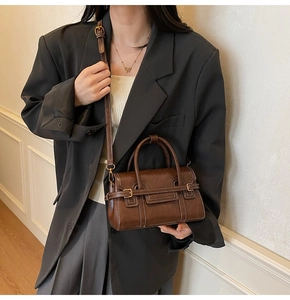 Dettaglio borsa a tracolla vintage marrone scuro con cuciture bianche e fibbia in metallo