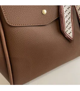 Détail d'un sac cabas marron en cuir grainé avec fermoir doré et foulard décoratif