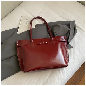 Close-up of deep red glossy patent leather tote bag with silver rivet studs