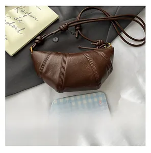 Detail of dark brown croissant bag with pleated wax texture on minimalist grey fabric