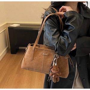 Brown suede tote bag detail with vertical stitching and cute teddy bear charm