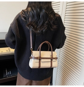 Dettaglio di una borsa a tracolla beige e marrone indossata da una modella in interni