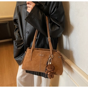 Close-up of brown suede tote bag with a plush bear charm and metal logo detail