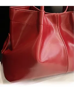 Detailed macro view of soft dark red leather texture and fine stitching on the tote bag