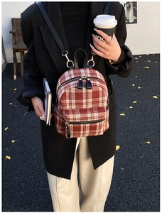 Close-up of red and white plaid tweed backpack featuring gold zippers and black leather straps