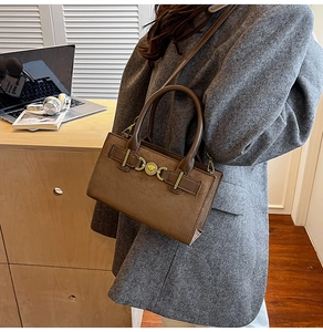 Detail of a brown suede handbag with heart clasp on a desk with office accessories