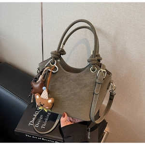 Detail of olive green bucket bag featuring a knotted handle and brown plush bear charm