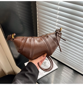 Detail of dark brown croissant bag with segmented stitching and knotted shoulder strap