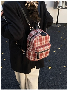 Detail of red checkered backpack with gold buckles on ginkgo leaves background