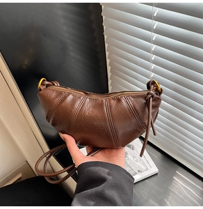 Detail of a brown leather croissant bag with pleated texture and gold ring hardware