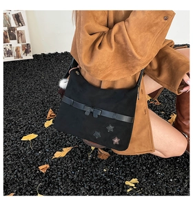 Detail of black suede shoulder bag with star embroidery and white pompom pendant