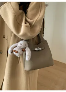 Detail of khaki leather bucket bag with metal twist lock and cute plush rabbit charm