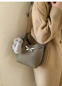 Detail view of taupe pebbled leather bucket bag with silver clasp and plush bunny charm