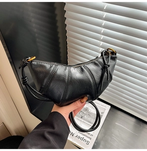 Detail of black leather croissant bag with stitch pleats and golden metal ring hardware