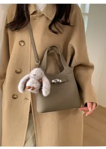 Detail of taupe leather bucket bag with metal clasp and cute plush rabbit charm