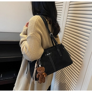 Close-up of black tote bag featuring white contrast stitching and cute plush bear charm