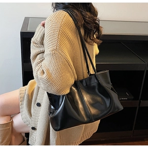 Detail of a black pleated leather tote bag with slender straps worn by a model