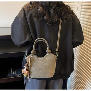 Detail of taupe bucket bag with cylindrical handles and cute brown bear charm accessory