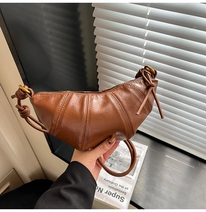 Detailed macro view of the brown leather croissant bag with elegant pleated texture and strap