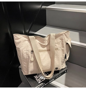 Detail of a large beige nylon tote bag with functional pockets and side zipper accents
