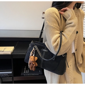 Detail of black matte tote bag featuring white contrast stitching and a plush bear charm