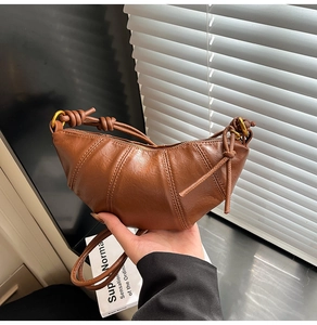 Detail of a brown leather croissant bag with knotted strap and rustic metal ring