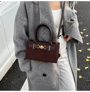 Detail of burgundy suede leather handbag featuring a gold heart lock and a top handle