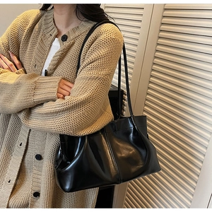 Detailed view of black pleated shoulder bag worn with beige cardigan for casual look