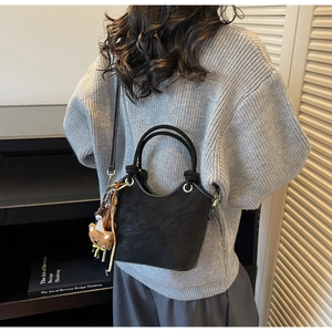 Detail of black suede bucket bag with white contrast stitching and a cute bear charm